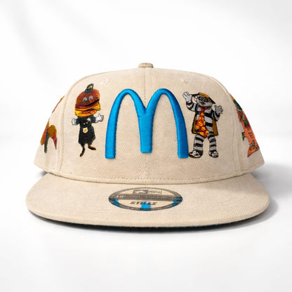 Beige cap with colorful graphics and blue 'M' logo on a white background